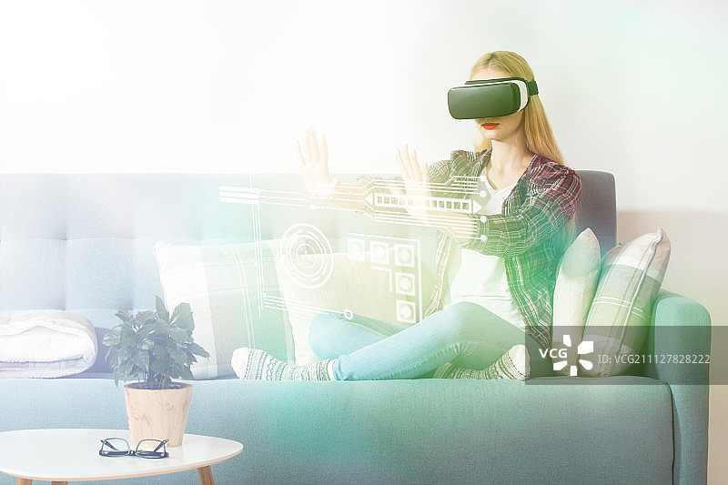 迷人的女人戴着虚拟现实眼镜坐在沙发上。虚拟现实耳机……图片素材