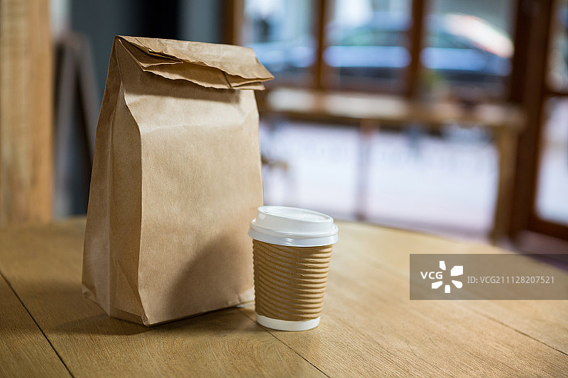 特写的一次性咖啡杯和纸袋在桌子上的咖啡馆图片素材