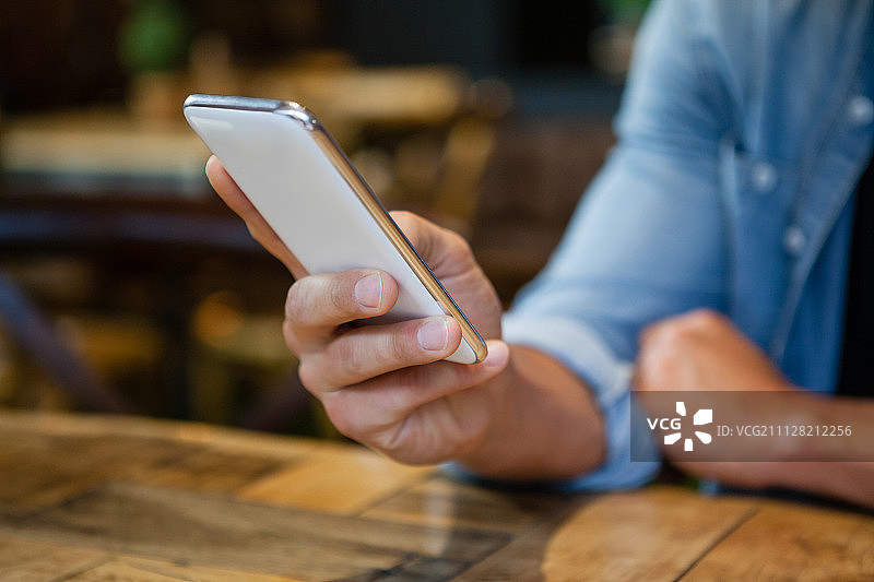 一名男子坐在咖啡馆的桌边使用智能手机图片素材