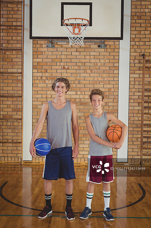 微笑的学校男孩拿着篮球在球场上的肖像图片素材