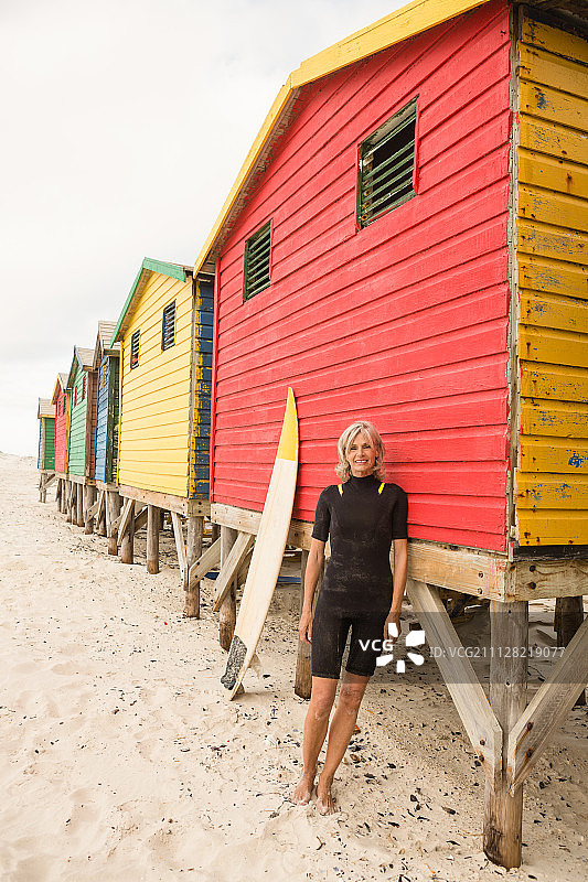 一位老妇人的肖像，她站在海边的红色小屋旁，映衬着天空图片素材