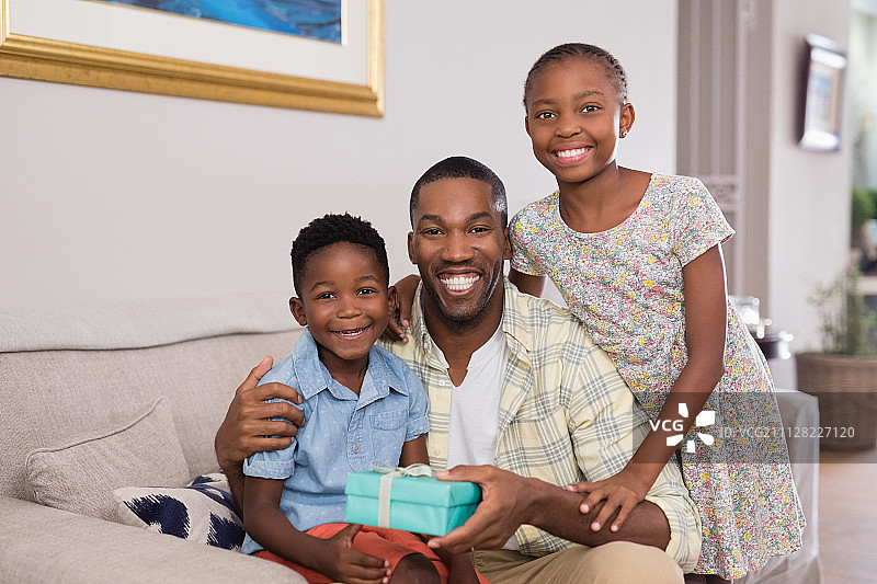 在家里的沙发上，微笑的父亲和孩子们拿着礼盒图片素材