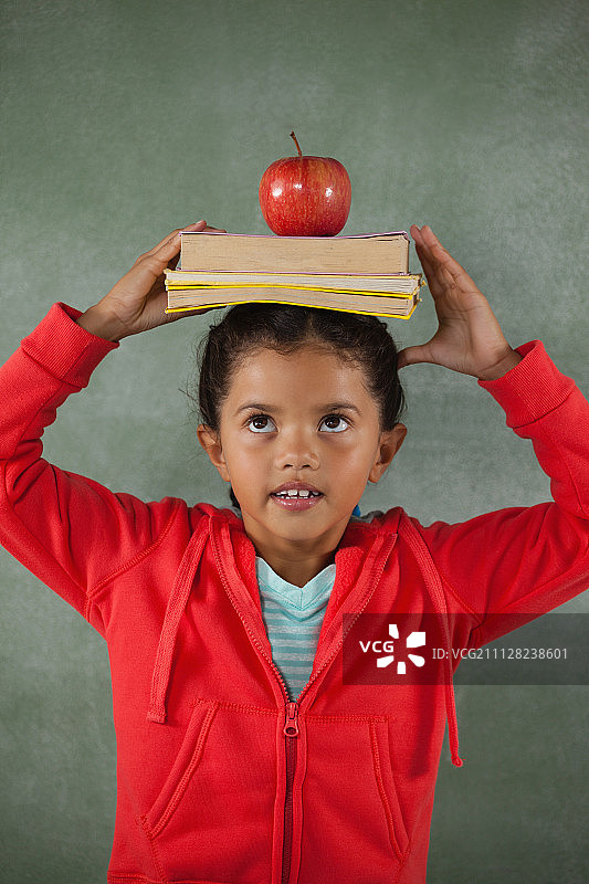 一个年轻的女孩用头顶着黑板平衡着书本和苹果图片素材