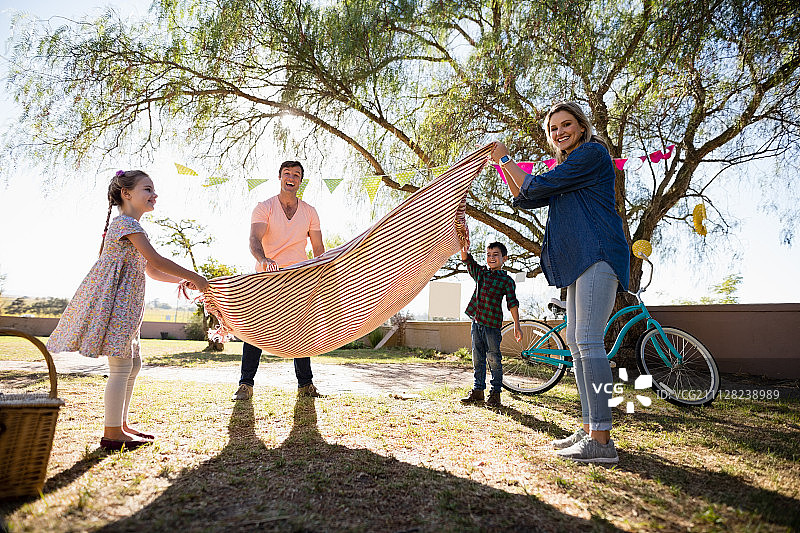 在一个阳光明媚的日子里，快乐的一家人在公园里放野餐毯图片素材