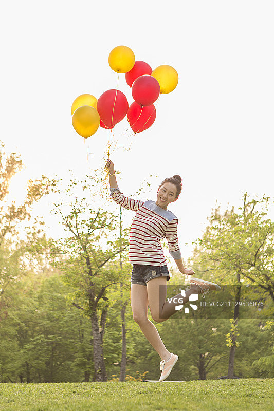 年轻女子拿着气球在公园跳伞图片素材