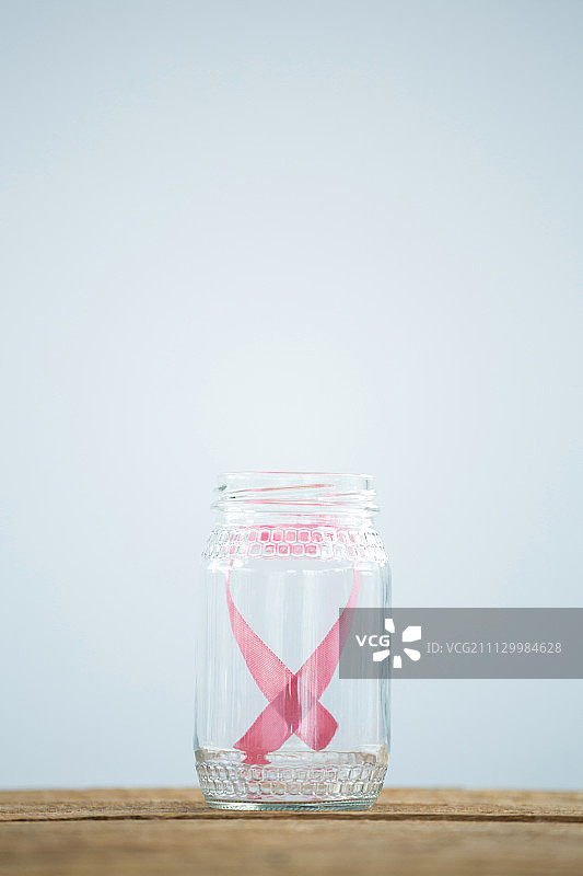 白色背景的桌子上，玻璃罐中粉红色的乳腺癌宣传丝带特写图片素材