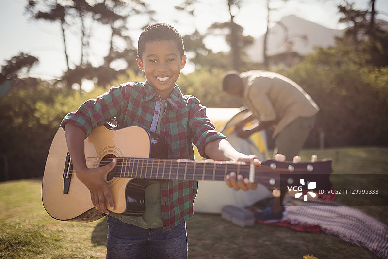 在一个阳光明媚的日子里，一个微笑的男孩在公园里弹吉他图片素材
