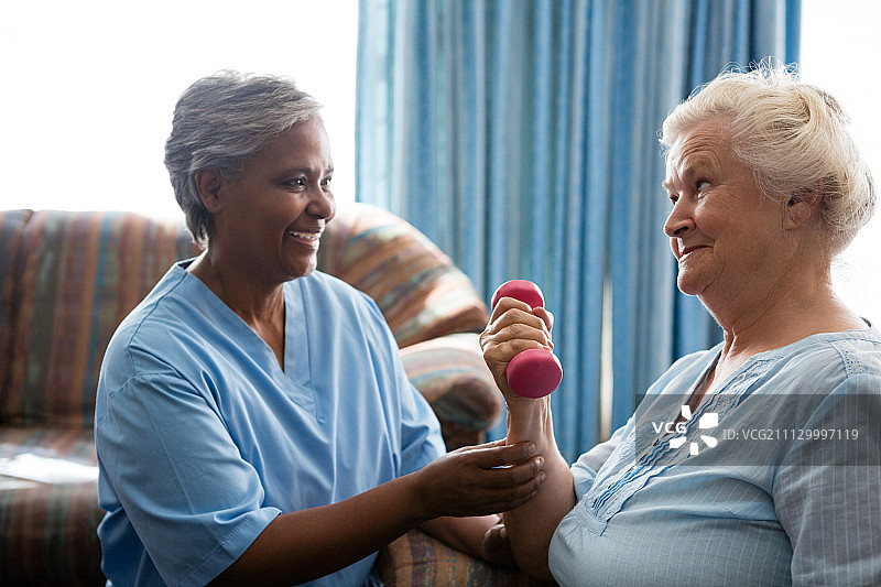 微笑的护士看着老女人举着哑铃在疗养院图片素材