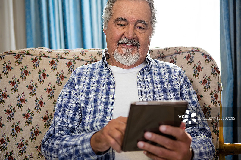 微笑的老人在疗养院的沙发上使用数字平板电脑图片素材