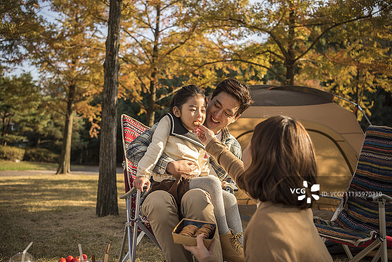 秋天，一家人坐在折叠椅上野餐，母亲在公园里喂女儿图片素材
