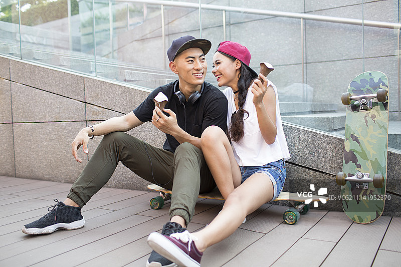 快乐的年轻情侣坐在滑板上吃冰淇淋图片素材