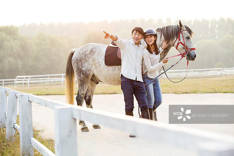 快乐的年轻情侣牵着马看向远方图片素材