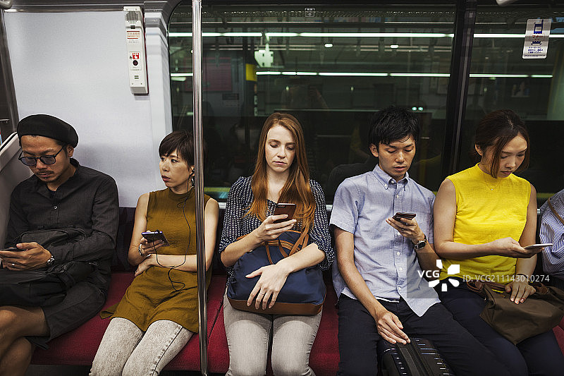 五个人并排坐在地铁上，东京通勤者。图片素材