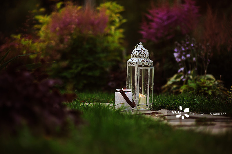 舒适的傍晚花园场景与复古灯笼和烛台草坪和鲜花的背景图片素材