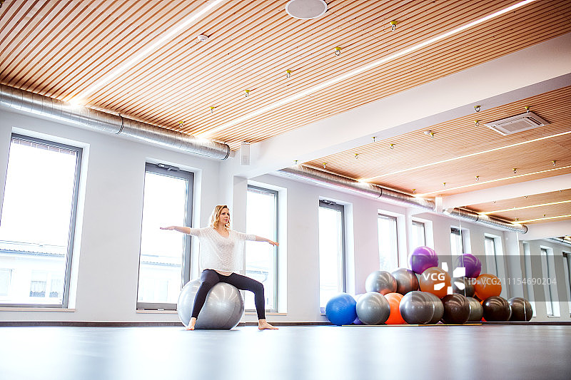 一名年轻女子在健身房里用健身球做运动。图片素材