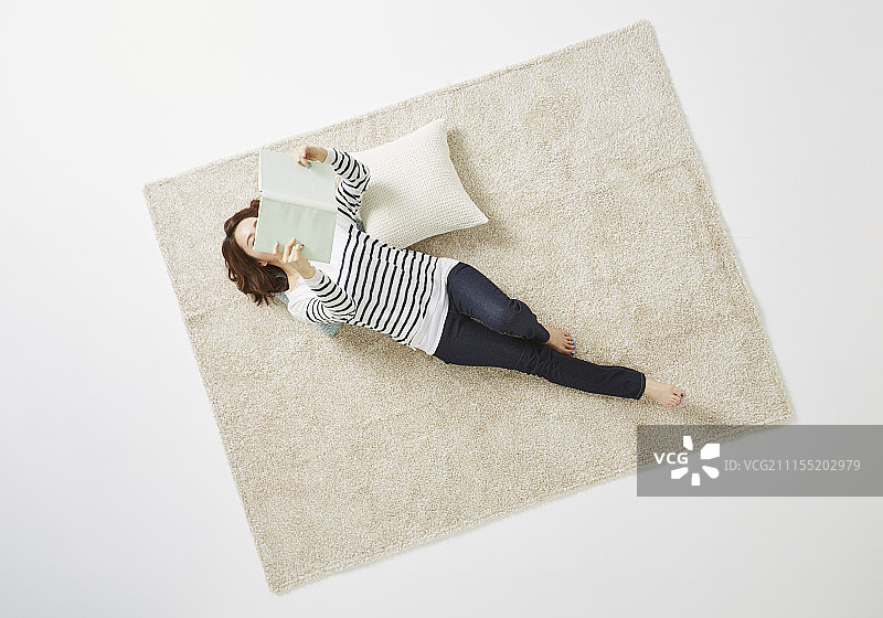 女人躺在地毯上看书的照片图片素材