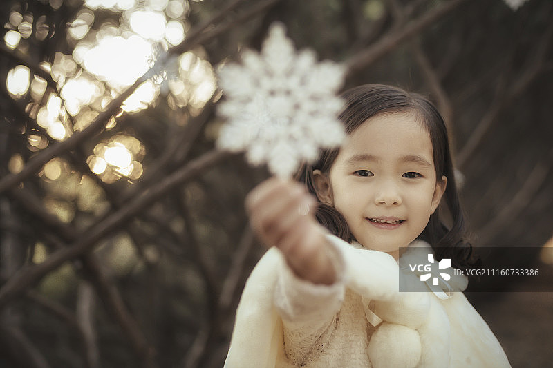 小女孩拿着雪花装饰站在街道上的照片图片素材