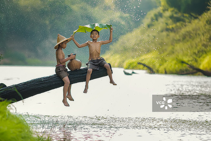 两个亚洲男孩在雨天站在树枝上图片素材