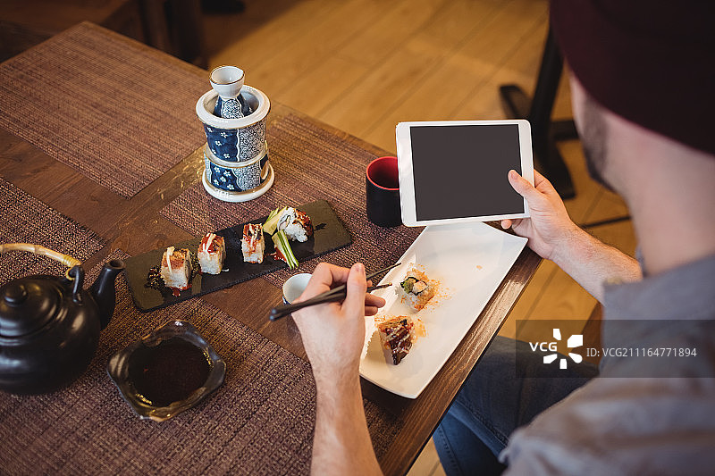 一名男子一边吃寿司一边使用电子平板电脑图片素材