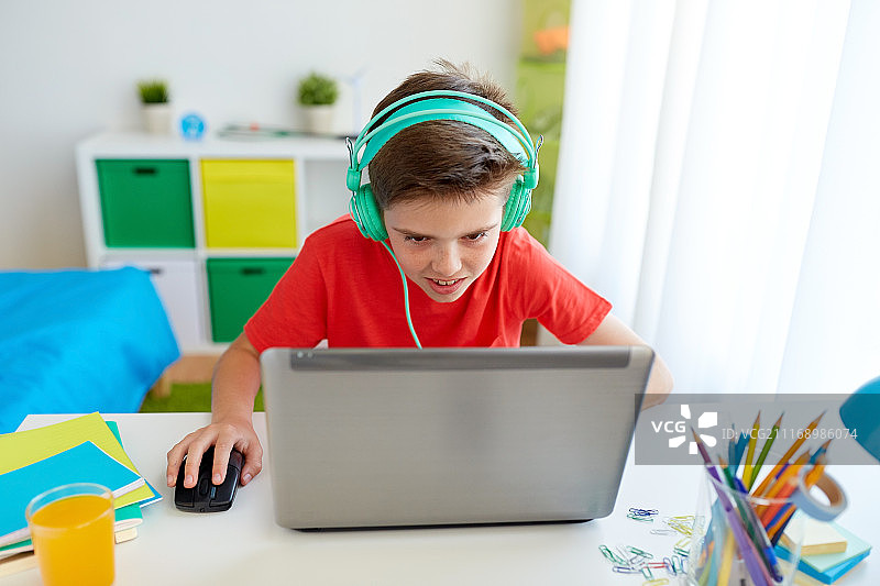 网络欺凌、游戏和人们的概念——男孩戴着耳机在家里的笔记本电脑上玩视频游戏。男孩戴着耳机在笔记本电脑上玩游戏图片素材