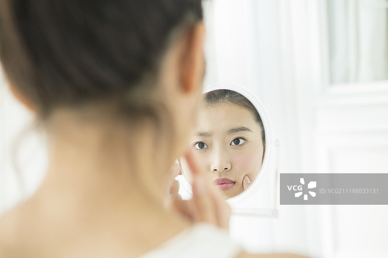 年轻女子看着镜子里自己的脸图片素材