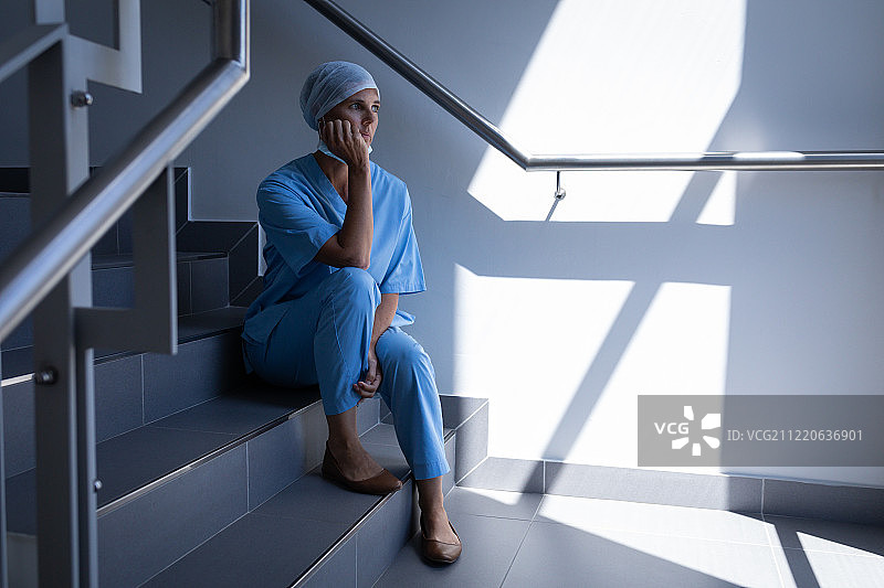 一个深思熟虑的女外科医生坐在楼梯上，抱着她的头在医院图片素材