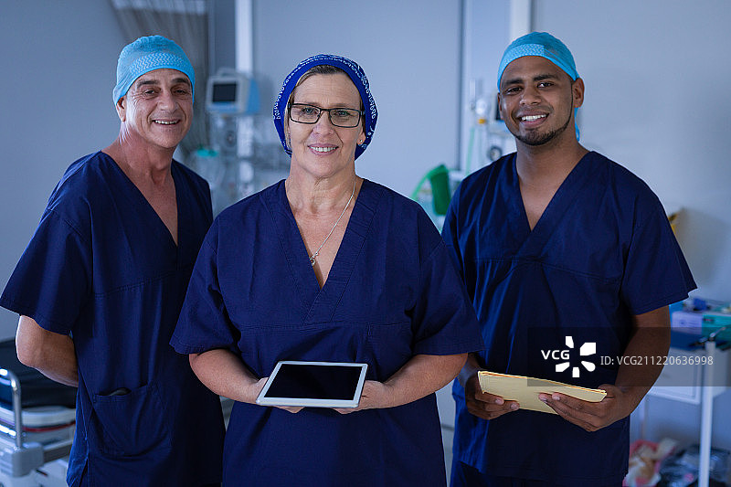 多民族外科医生对着镜头微笑，而站在医院诊所的数字平板电脑和文件夹图片素材