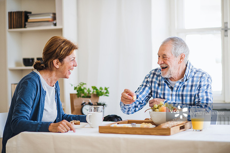 一对老年夫妇坐在家里的桌子旁，吃早餐。图片素材