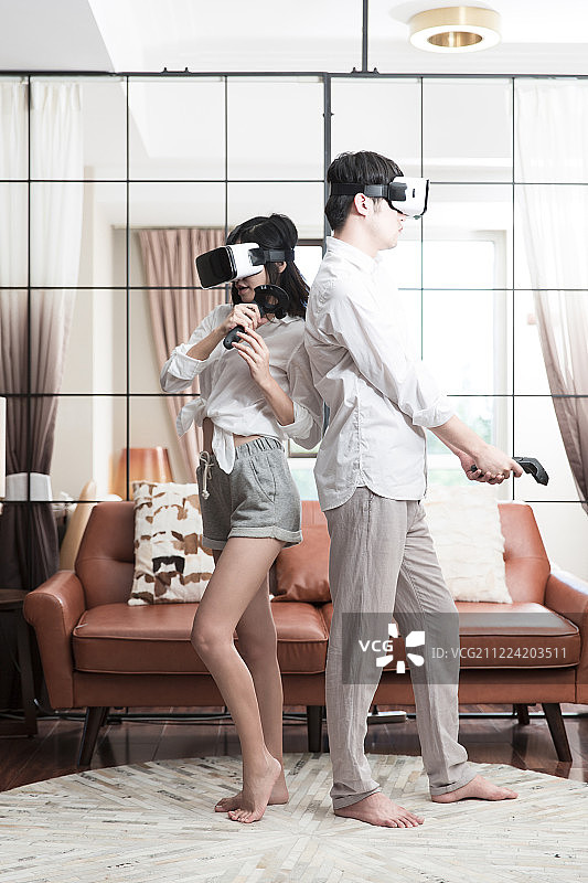 青年情侣在起居室一起玩VR虚拟游戏图片素材