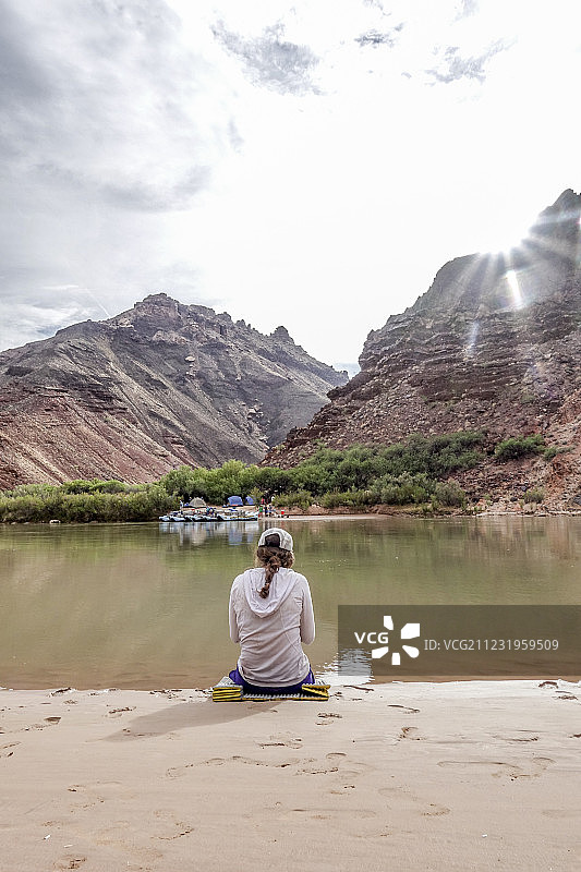女性徒步旅行者坐在科罗拉多河岸边的后视图，在大峡谷，美国亚利桑那州图片素材
