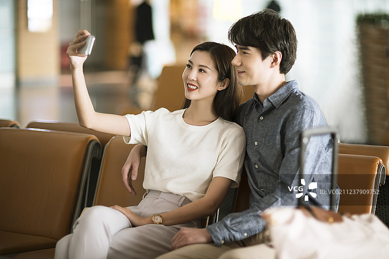 年轻情侣在机场候机室使用手机自拍图片素材