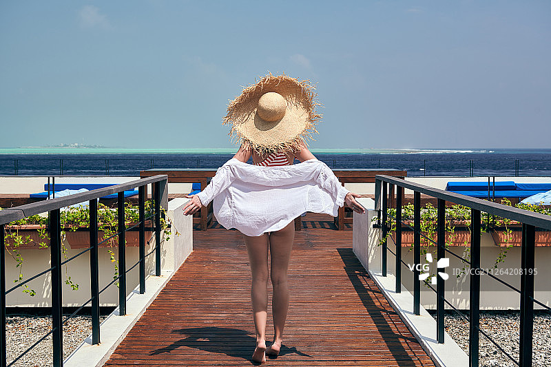 女人在红色条纹泳衣走在热带海滩露台甲板。暑假在马尔代夫。图片素材