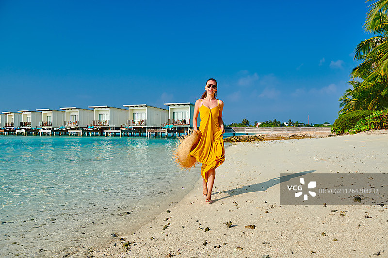 穿着衣服的女人在热带海滩上跑步。暑假在马尔代夫。图片素材