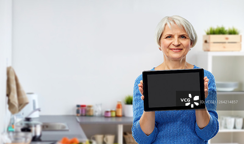 技术和老年人的概念-微笑的妇女使用平板电脑在厨房的背景。妇女在厨房里使用平板电脑图片素材