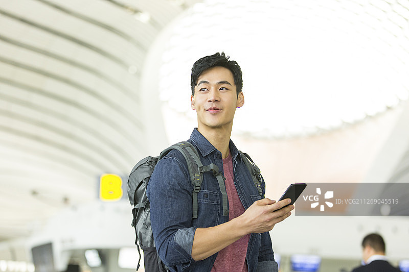 背包的青年男子使用手机在机场图片素材