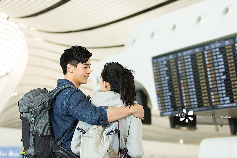 青年情侣在机场看显示屏核对飞机航班信息图片素材