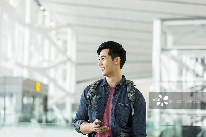青年男子背着包使用手机在机场等候图片素材