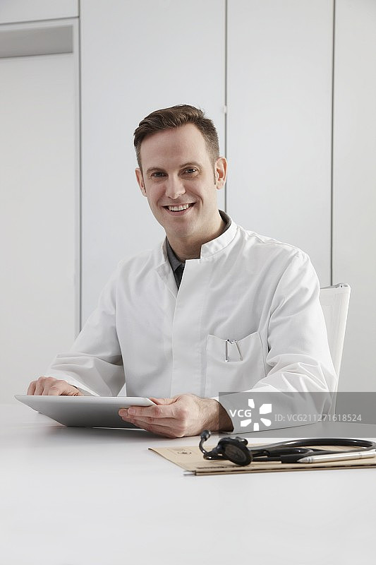 医生的肖像坐在书桌与数字平板电脑图片素材