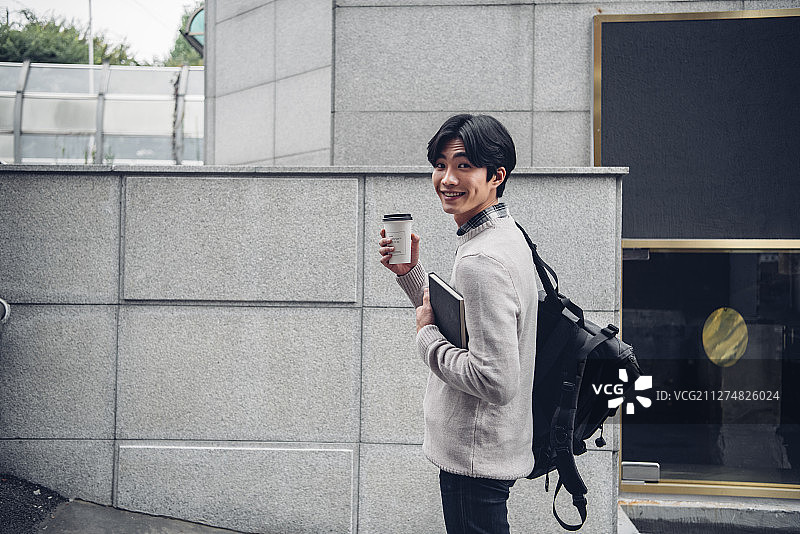 一个男人拿着咖啡走在街上的照片图片素材
