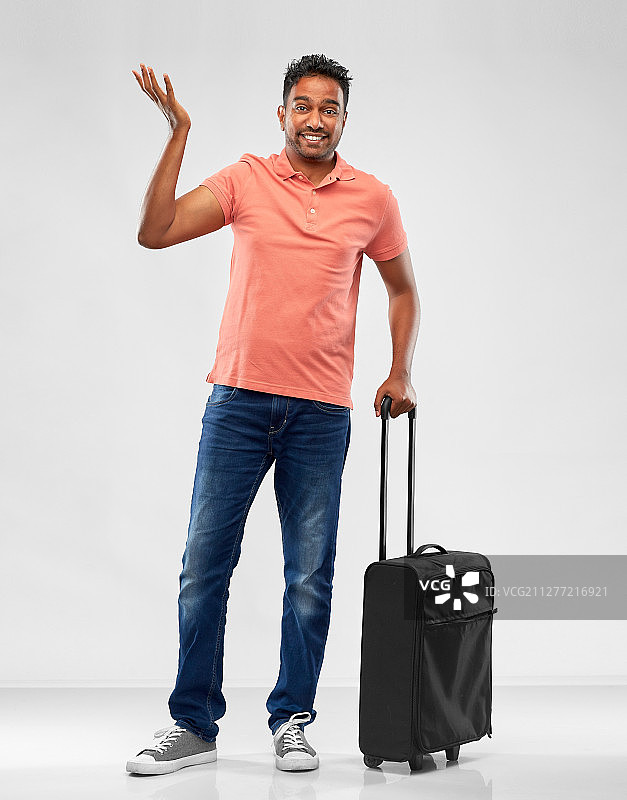 家庭，旅游和度假的概念-困惑的印度男子polo衫与旅行袋肩在灰色的背景。印度男人在马球衫与旅行袋耸肩图片素材