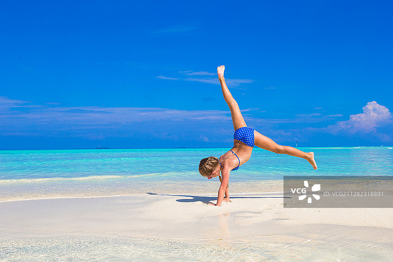 可爱的小女孩玩Cartwheel在热带白色沙滩上图片素材