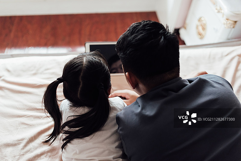 一对亚洲父女正在床上使用平板电脑图片素材