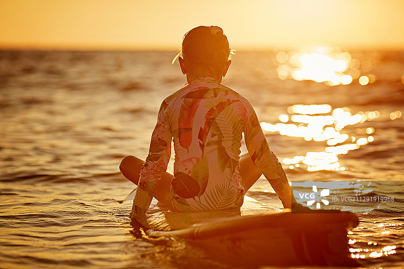 小女孩(8-9岁)在日落时坐在冲浪板上图片素材