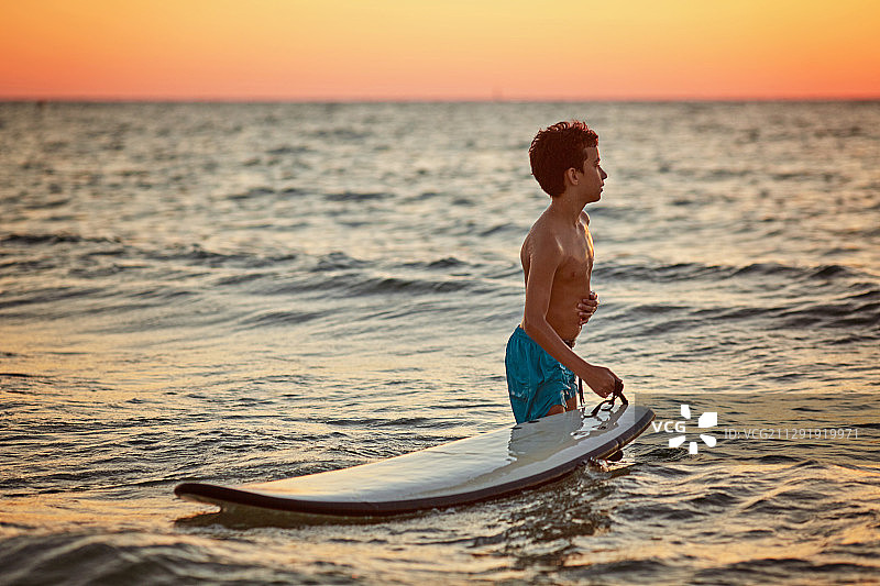 赤膊男孩与冲浪板在日落的海上图片素材