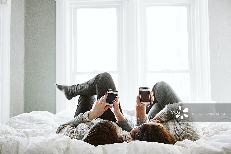 两个躺在床上玩手机的女人图片素材