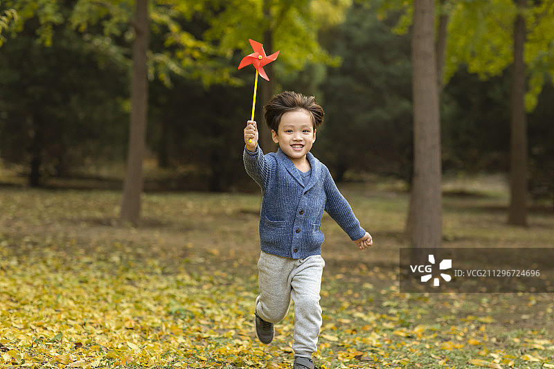 快乐的小男孩在树林里玩玩具风车图片素材