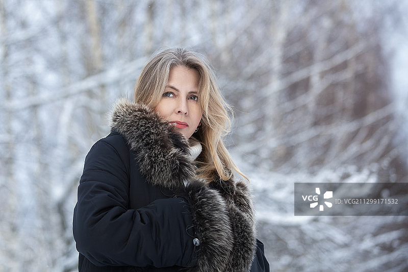 肖像的女人穿着暖和的衣服，而站在光秃秃的树木在冬天图片素材