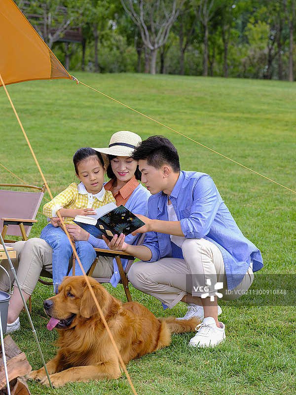 快乐的三口之家和宠物狗在户外看书图片素材
