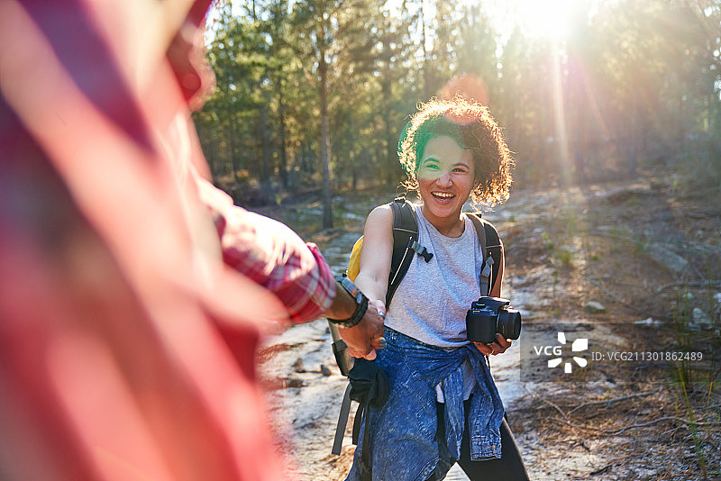 快乐的年轻夫妇带着相机在阳光明媚的树林里徒步旅行图片素材