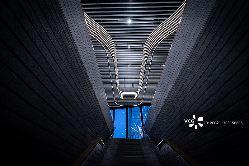 建筑物内部V字型的楼梯和灯光结构，远处是蓝色的天空图片素材